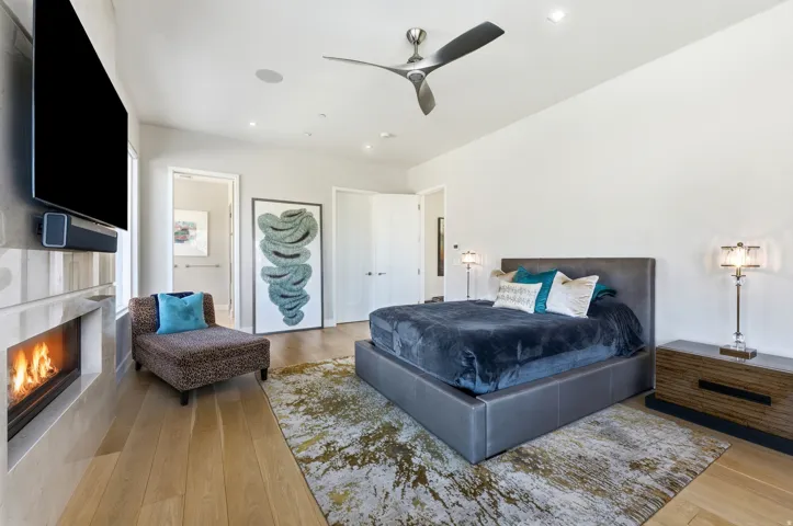 Spacious room featuring wood-finish flooring, a wall-mounted fireplace with an integrated television, and a contemporary ceiling fan