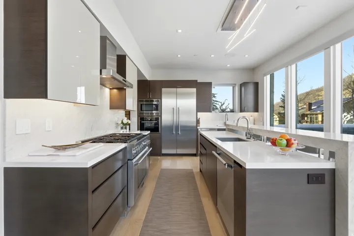 Modern kitchen featuring wood-finish lower cabinetry, white upper cabinetry, and a full suite of stainless steel appliances