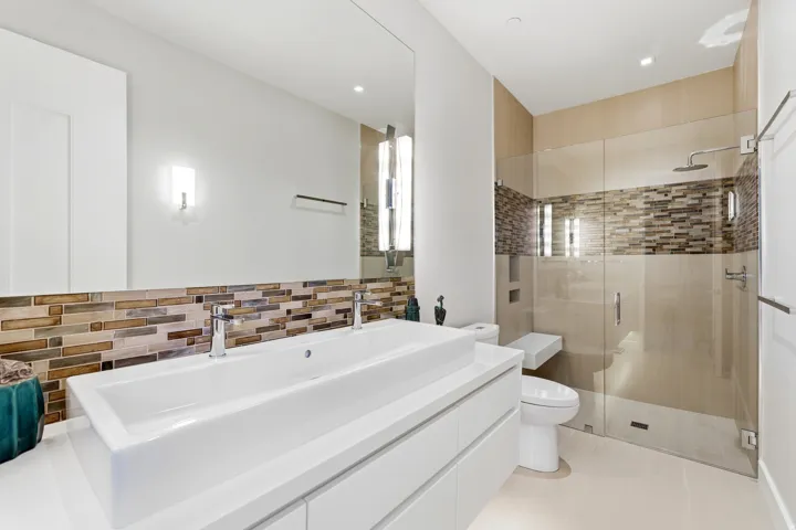Contemporary bathroom featuring a dual vanity with rectangular vessel sinks, extensive mirrored wall, glass-enclosed shower with a built-in bench, and a mosaic tile accent band