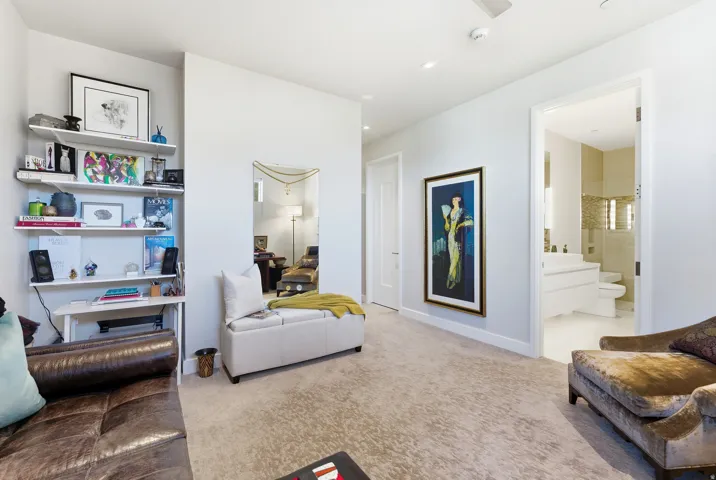 Plush carpeting throughout this interior space, featuring a built-in shelving unit, a neutral color palette, a doorway to an additional room, and a ceiling-mounted smoke detector