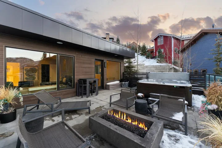 Modern outdoor patio featuring a built-in fire pit, a hot tub, and a large sliding glass door opening to the interior