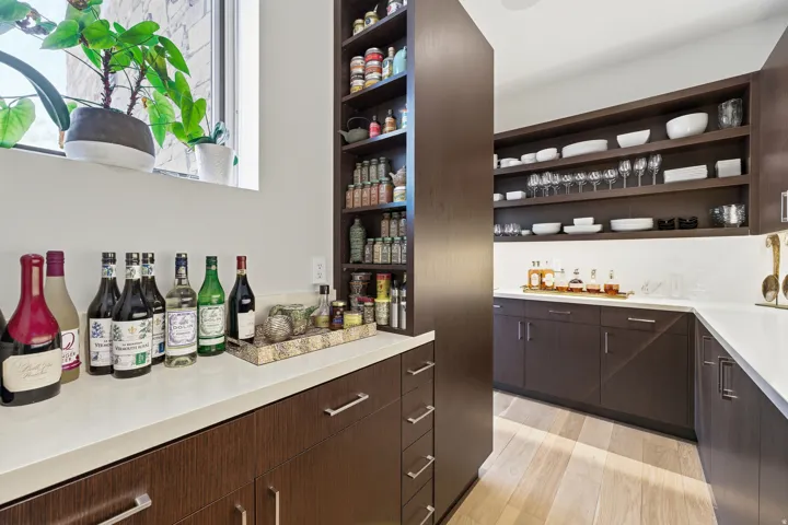 Custom pantry featuring extensive dark wood-finish cabinetry, light-toned countertops, open shelving, integrated shelving units, and a window with natural light