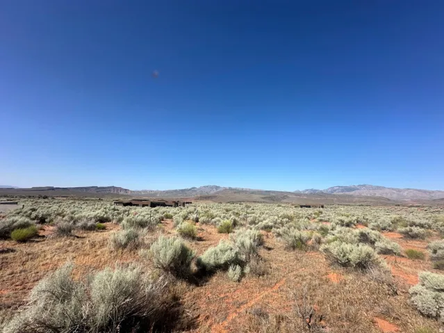 Expansive desert landscape featuring natural brush, reddish-brown ground cover, and distant mountains