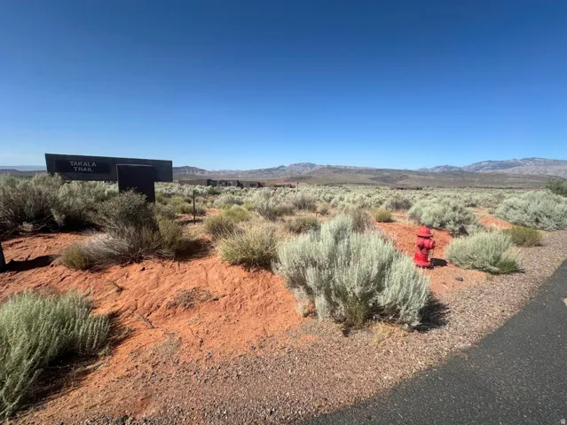 Red rock landscape featuring native vegetation, a paved road, and distant mountains