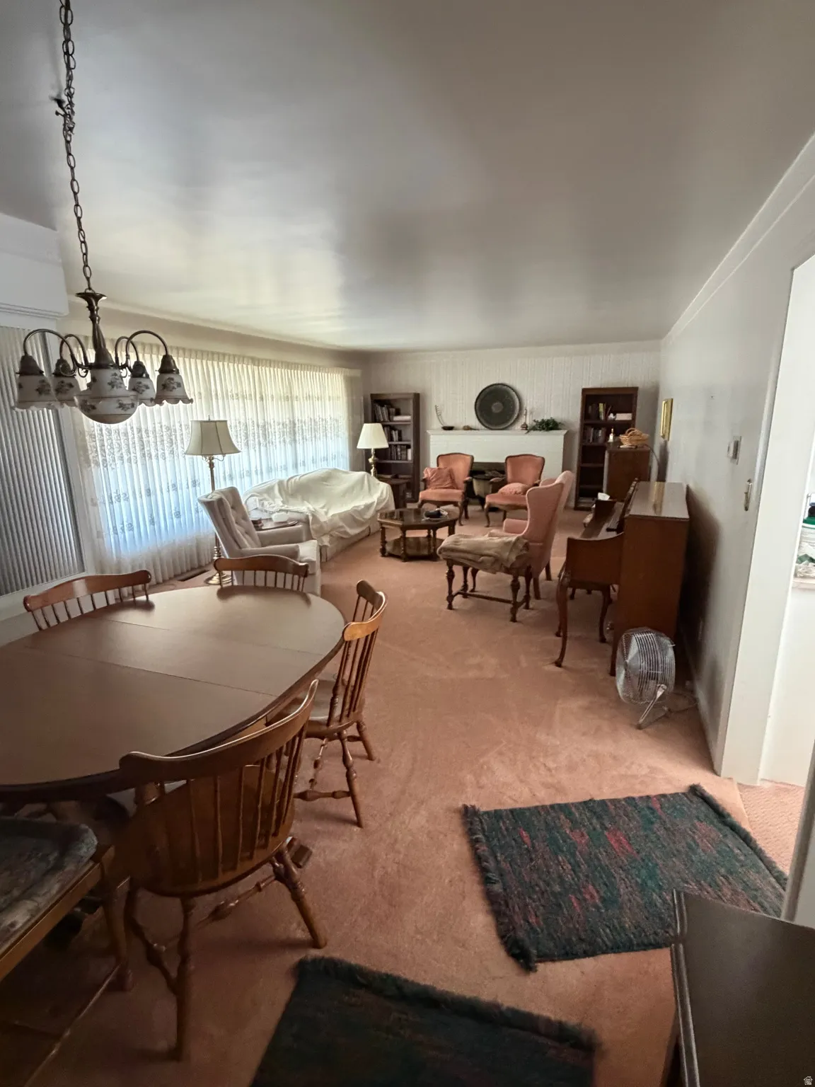 Spacious living area featuring wall-to-wall carpeting, a chandelier, and a large window with privacy sheers