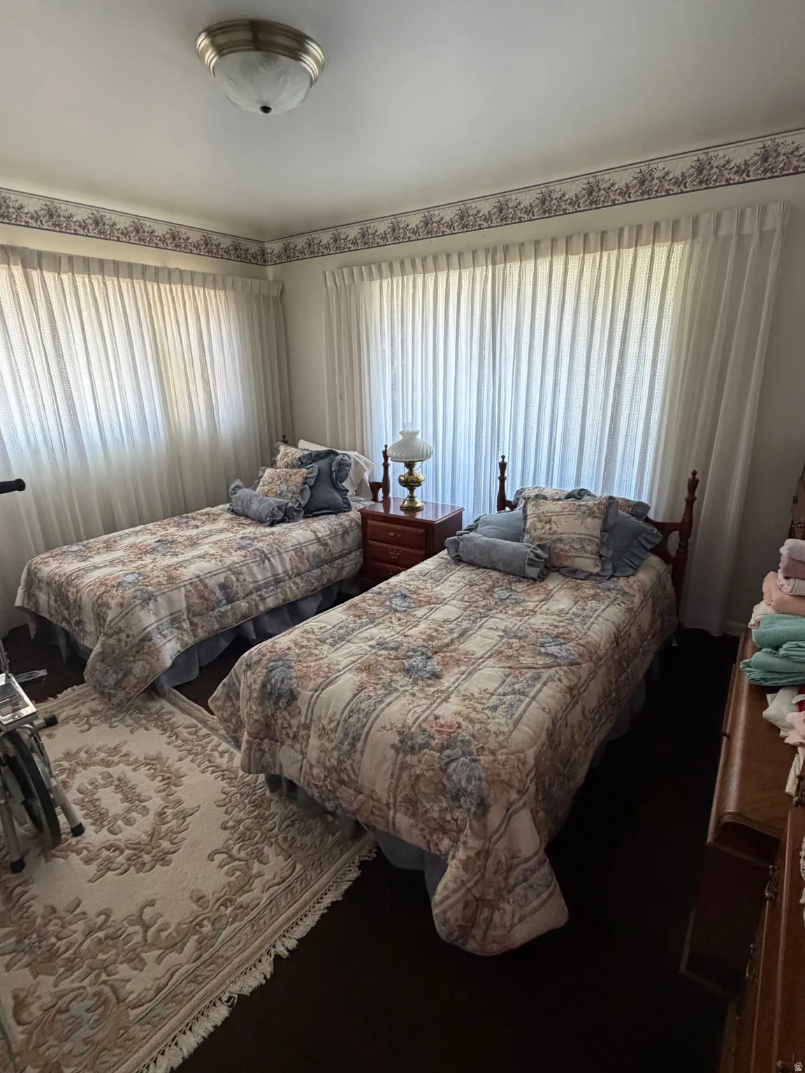 Room featuring dark wood-finish flooring and two large windows with sheer white curtains