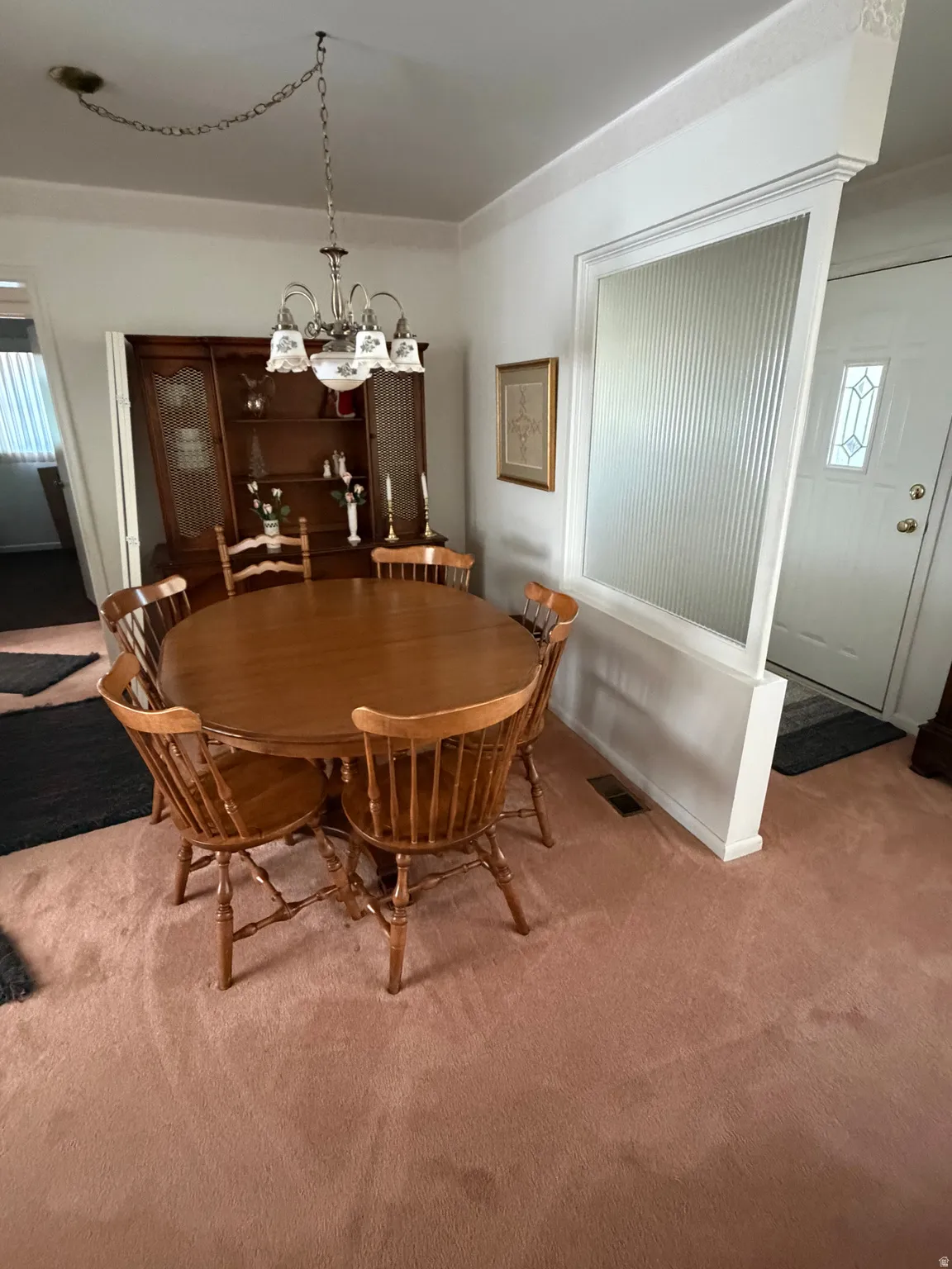 Dining area with a brass chandelier, a built-in display cabinet, and light pink carpeting