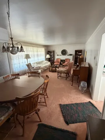 Spacious living area featuring wall-to-wall carpeting, a chandelier, and a large window with privacy sheers