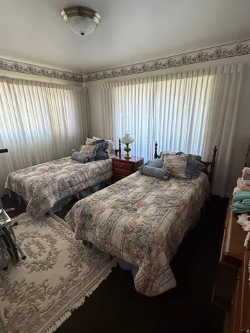 Room featuring dark wood-finish flooring and two large windows with sheer white curtains