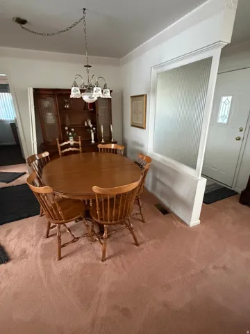 Dining area with a brass chandelier, a built-in display cabinet, and light pink carpeting