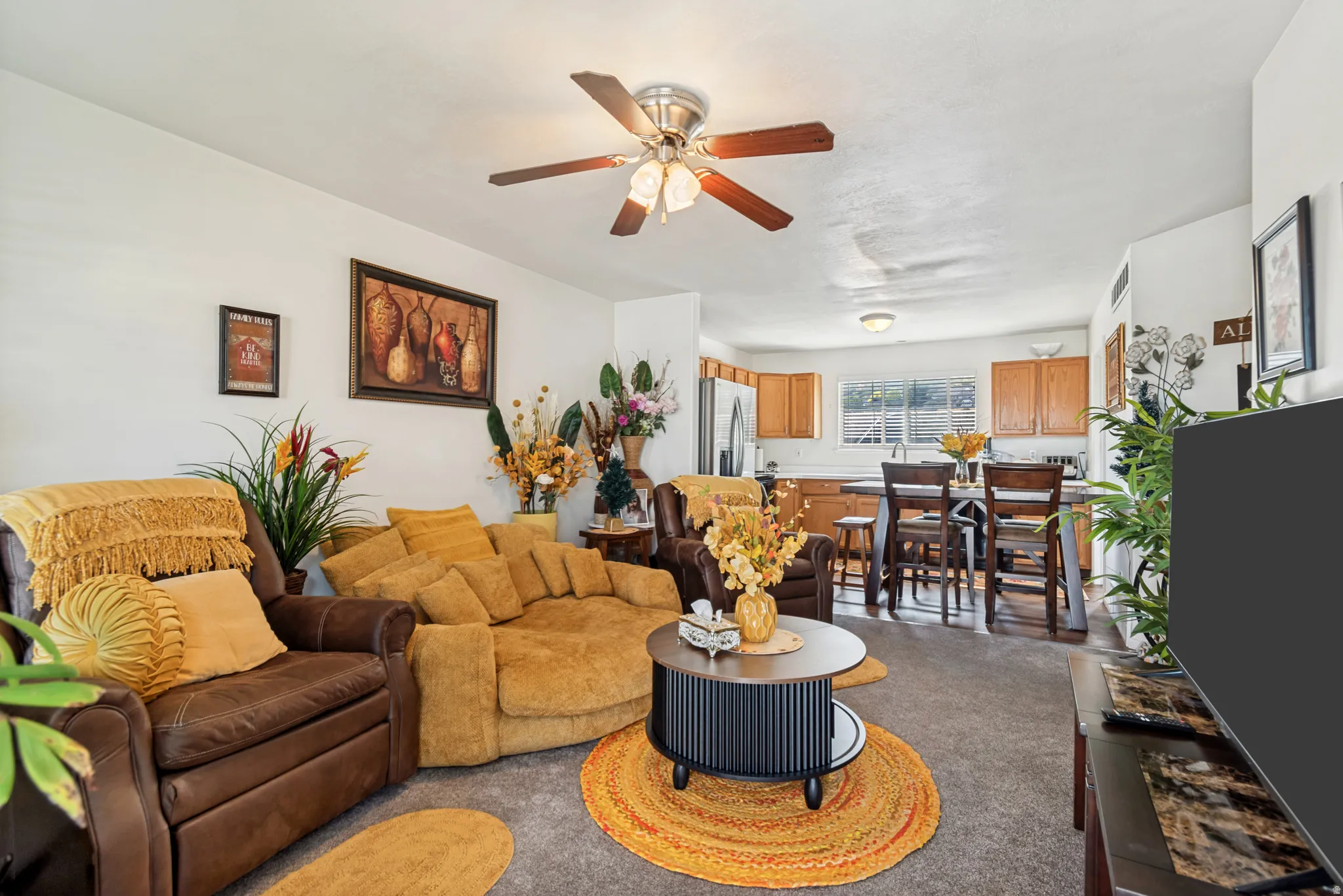 Open-concept living area with neutral carpeting, a ceiling fan with integrated lighting, and white walls