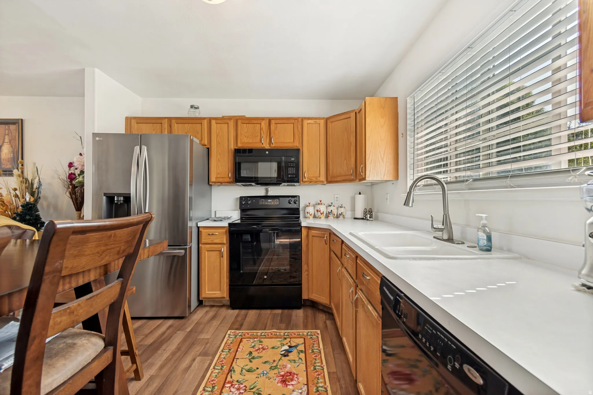 Kitchen featuring wood cabinetry, white countertops, stainless steel refrigerator, black range, and wood-finish flooring