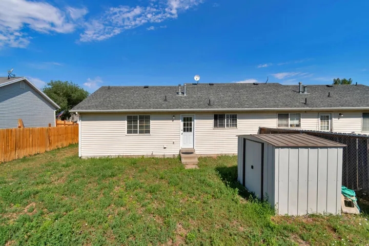 Expansive backyard featuring a full wooden fence, an exterior storage shed, and a rear entry door with step access