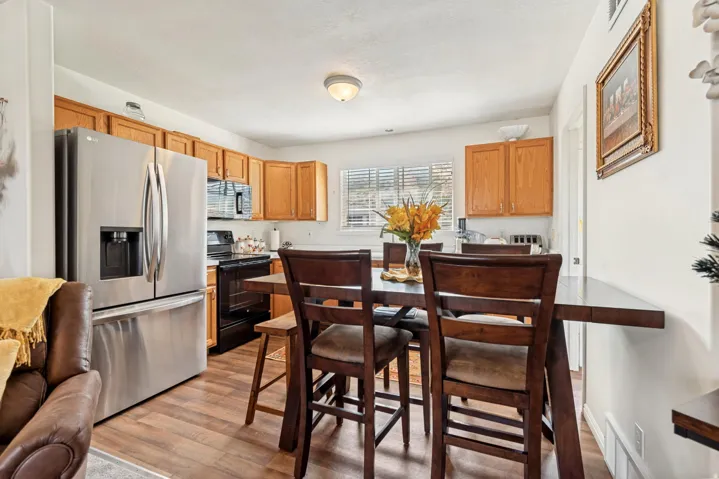 Kitchen dining area featuring wood-finish flooring, wood cabinetry, stainless steel refrigerator, black range, and a dining table with chairs