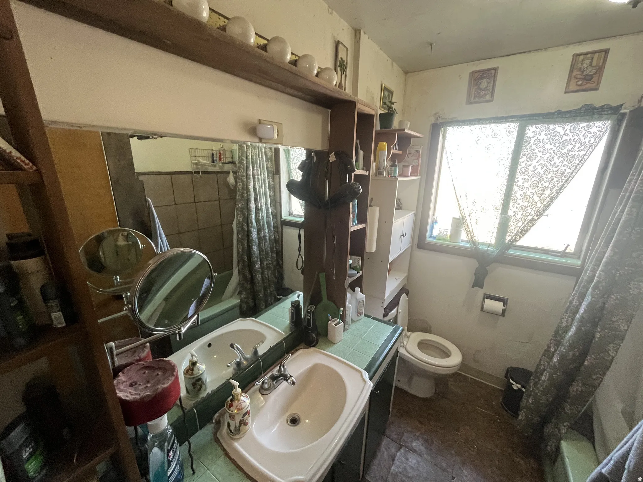 Bathroom featuring a double vanity with integrated sinks and green tiled countertop, a built-in shelf above the mirror, a window with natural light, and tiled flooring