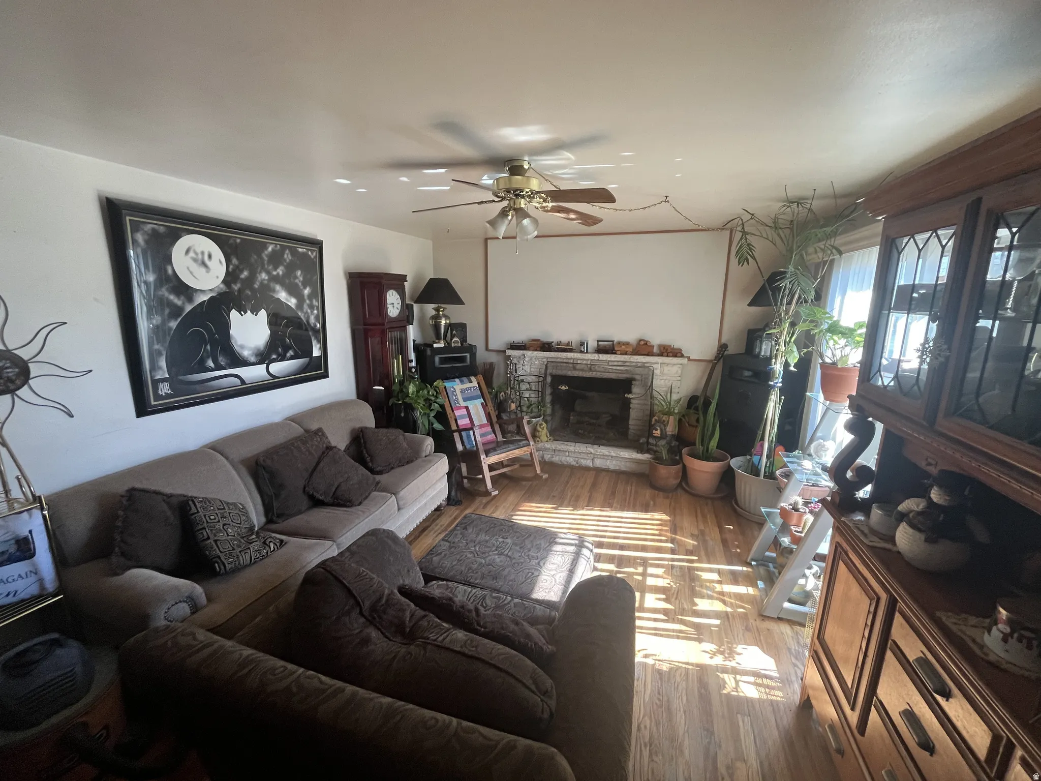 Living area featuring wood-finish flooring, a brick fireplace, and a ceiling fan