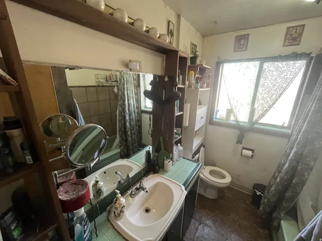 Bathroom featuring a double vanity with integrated sinks and green tiled countertop, a built-in shelf above the mirror, a window with natural light, and tiled flooring