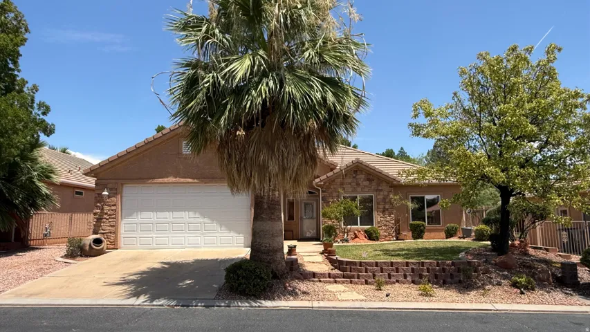 Stucco and stone facade home featuring an attached garage, paved driveway, and mature landscaping
