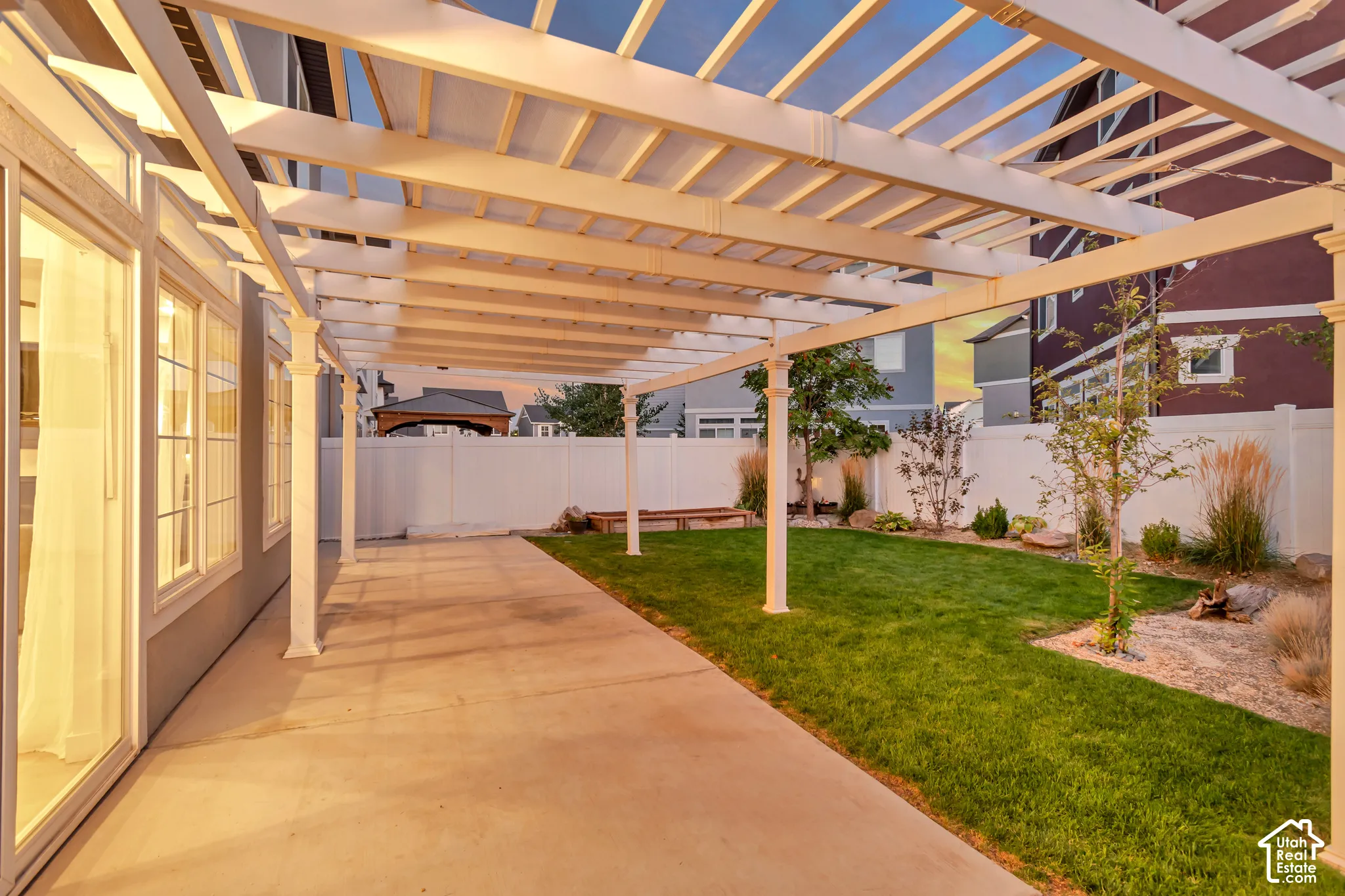 Expansive patio featuring a white pergola with translucent panels, concrete hardscaping, and a manicured lawn