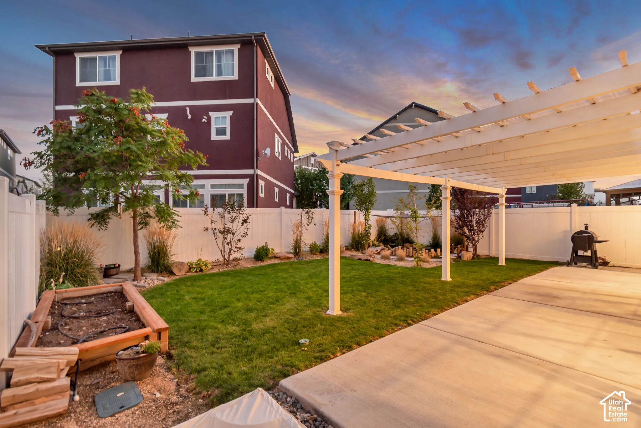 Expansive backyard featuring a white pergola, concrete patio, vibrant green lawn, and a raised garden bed
