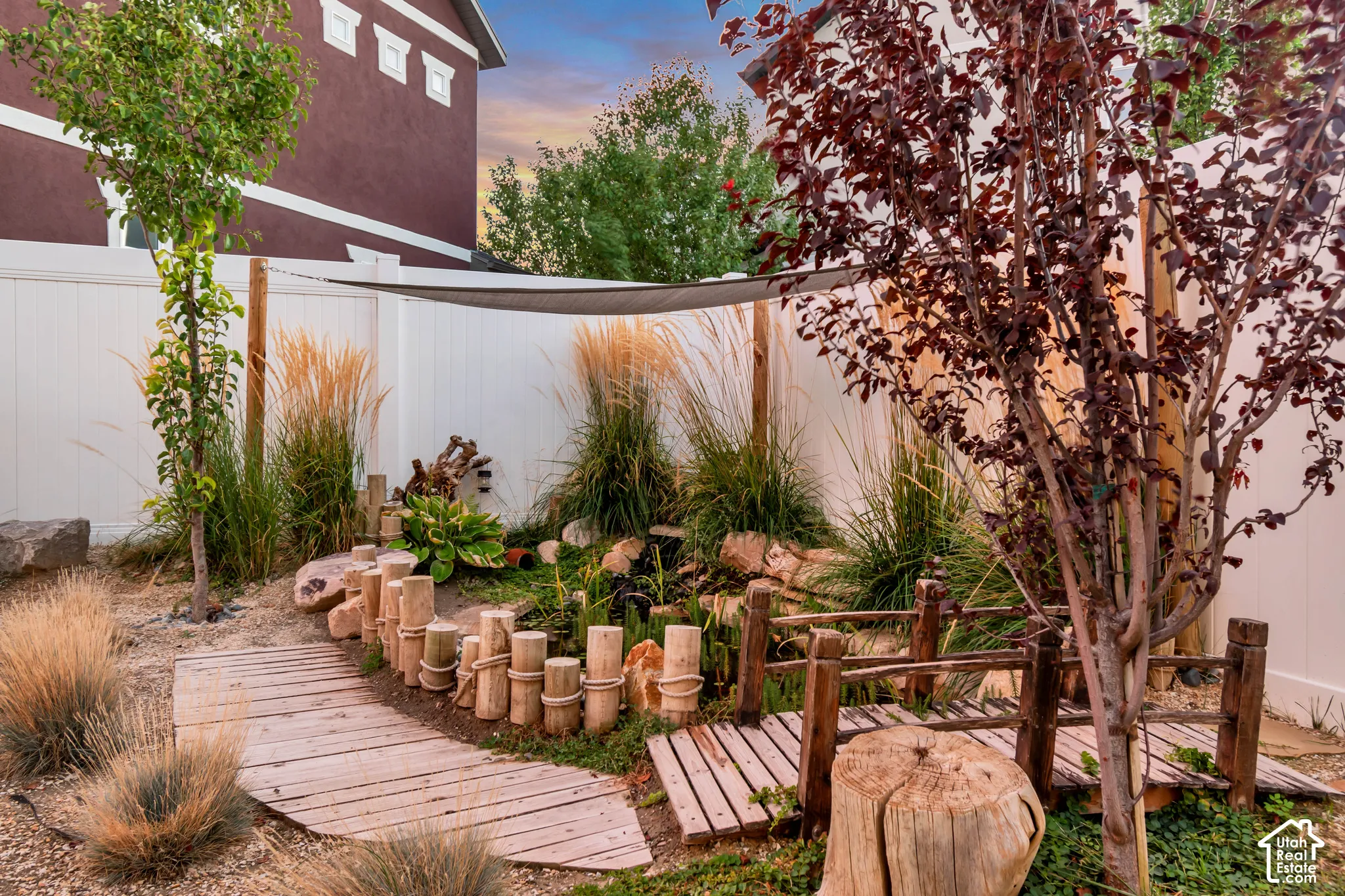 Landscaped backyard featuring a wooden walkway, decorative short fence, and mature trees