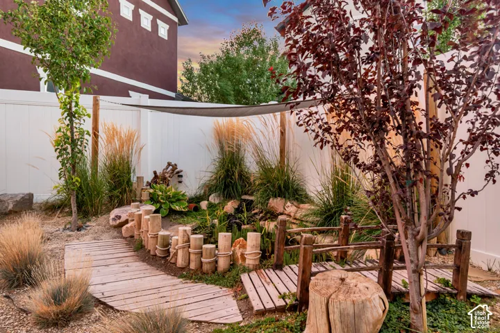 Landscaped backyard featuring a wooden walkway, decorative short fence, and mature trees