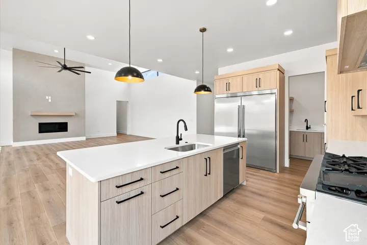 Open-concept kitchen with wood-finish flooring, a central island featuring a white countertop and integrated sink, stainless steel appliances, and a gas range