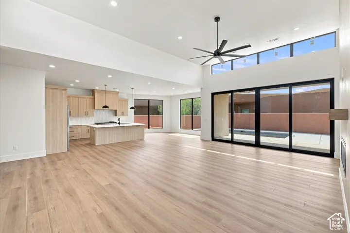 Vaulted ceiling with a contemporary ceiling fan, wood-finish flooring, sliding glass doors to outdoor hardscaping, recessed lighting, and kitchen with light wood cabinetry and island