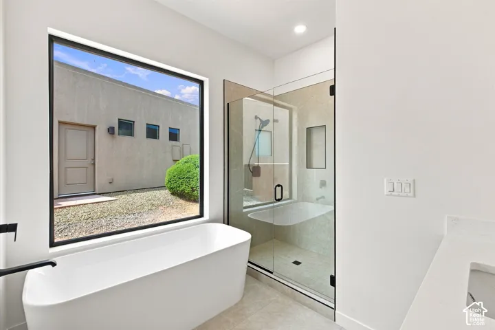 Freestanding soaking tub with a black wall-mounted faucet, walk-in shower with a glass enclosure, and a stone countertop vanity