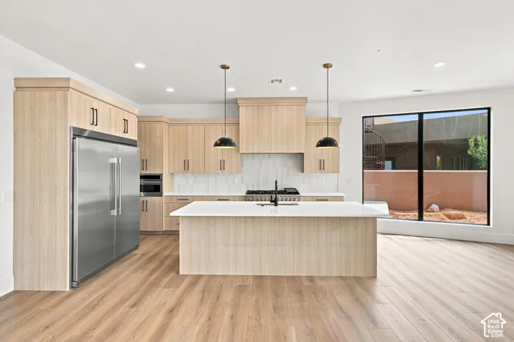 Spacious kitchen featuring light wood-finish cabinetry, stainless steel appliances, a center island with a white countertop, and a white tiled backsplash