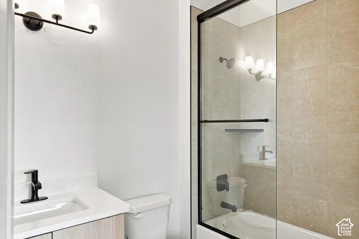 Bathroom featuring a glass-enclosed tub-shower with large format wall tiling, a vanity with a white countertop and integrated sink, and black fixtures