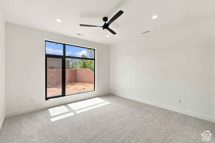 Expansive room featuring a large black-framed window, textured carpeting, recessed lighting, and a ceiling fan with wood-finish blades