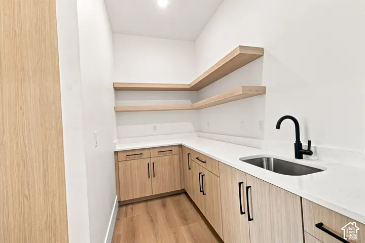 Wood-finish cabinetry with matte black hardware, white countertops, stainless steel sink, matte black faucet, and wood-finish open shelving
