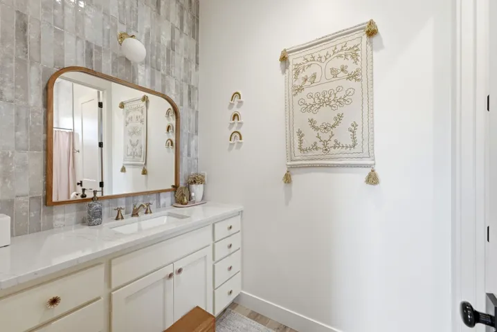 Bathroom vanity with a white countertop and integrated sink, featuring a wood-frame mirror and a tiled accent wall