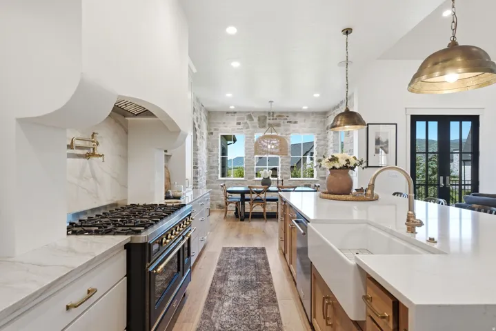 Expansive kitchen featuring a large island with a farmhouse sink, stone accent wall, wood-finish flooring, a range with a pot filler, and recessed lighting