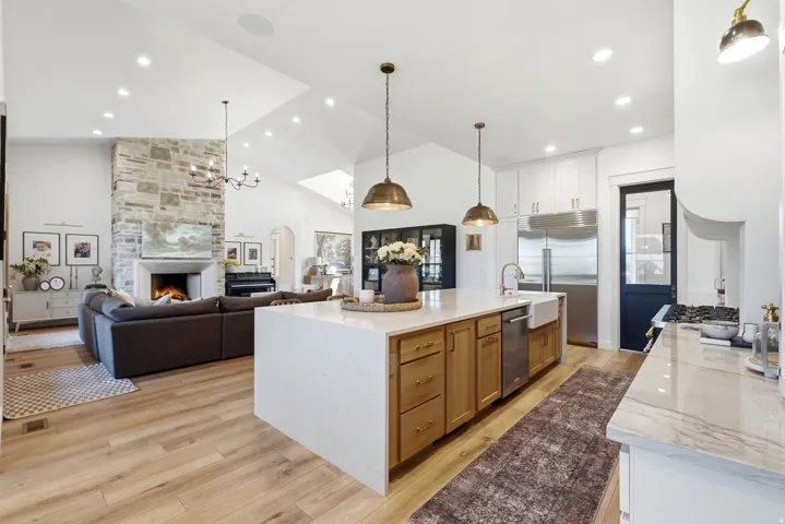 Gourmet kitchen featuring a large central island with light wood-finish cabinetry and a farmhouse sink, stainless steel appliances, and ceiling-mounted pendant lighting