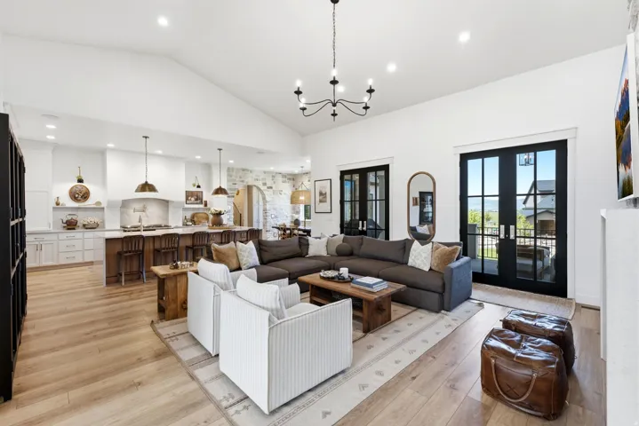 Open-concept living space featuring vaulted ceilings, light wood-finish flooring, a kitchen island with seating, and black-framed glass doors