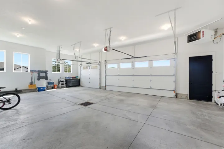 Spacious garage featuring a concrete floor, multiple windows, two overhead garage doors with window panels, recessed lighting, and a dark-paneled side door