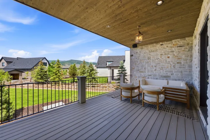 Expansive covered deck featuring composite decking, a stone accent wall, and a wood-paneled ceiling with recessed lighting