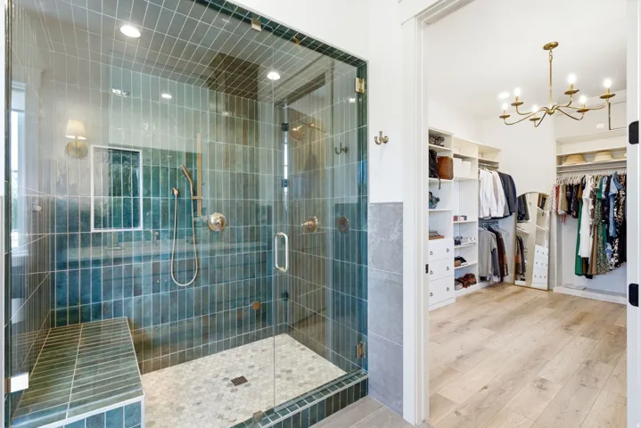 Spacious walk-in shower with a glass enclosure, vertical teal subway tile, a built-in bench, and a hexagonal mosaic tile floor