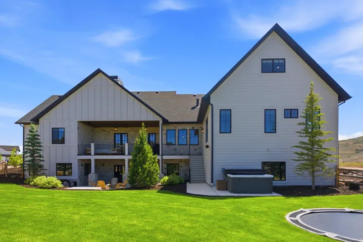 Rear exterior featuring a covered deck, lower patio, and a stone facade