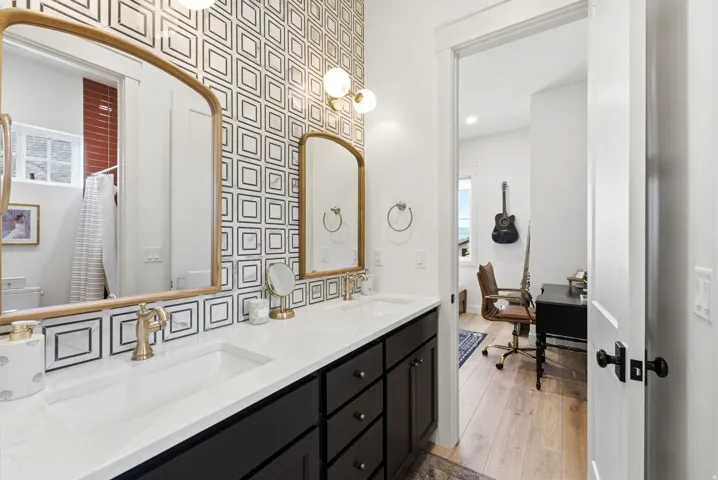 Dual vanity with integrated sinks, brushed gold fixtures, black cabinetry, and a geometric pattern accent wall