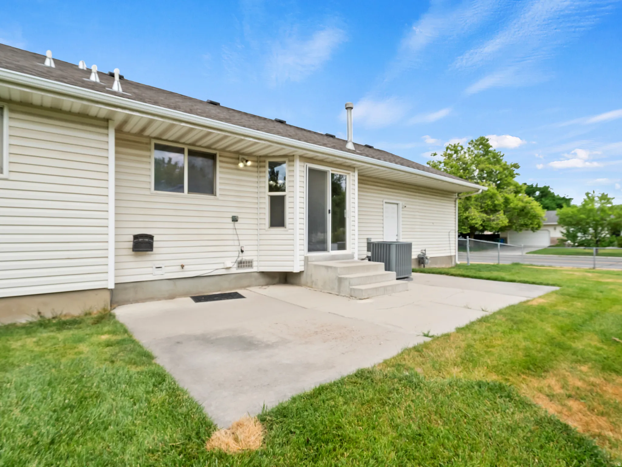 Rear exterior featuring vinyl siding, concrete patio, sliding glass door, and a grass lawn