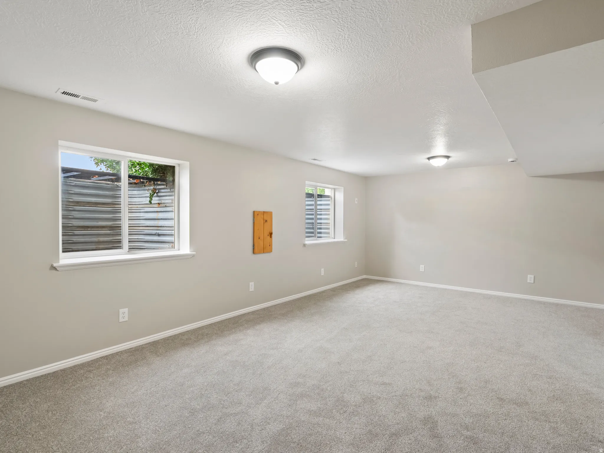 Spacious room featuring neutral paint, gray carpeting, white trim, and two windows with window wells