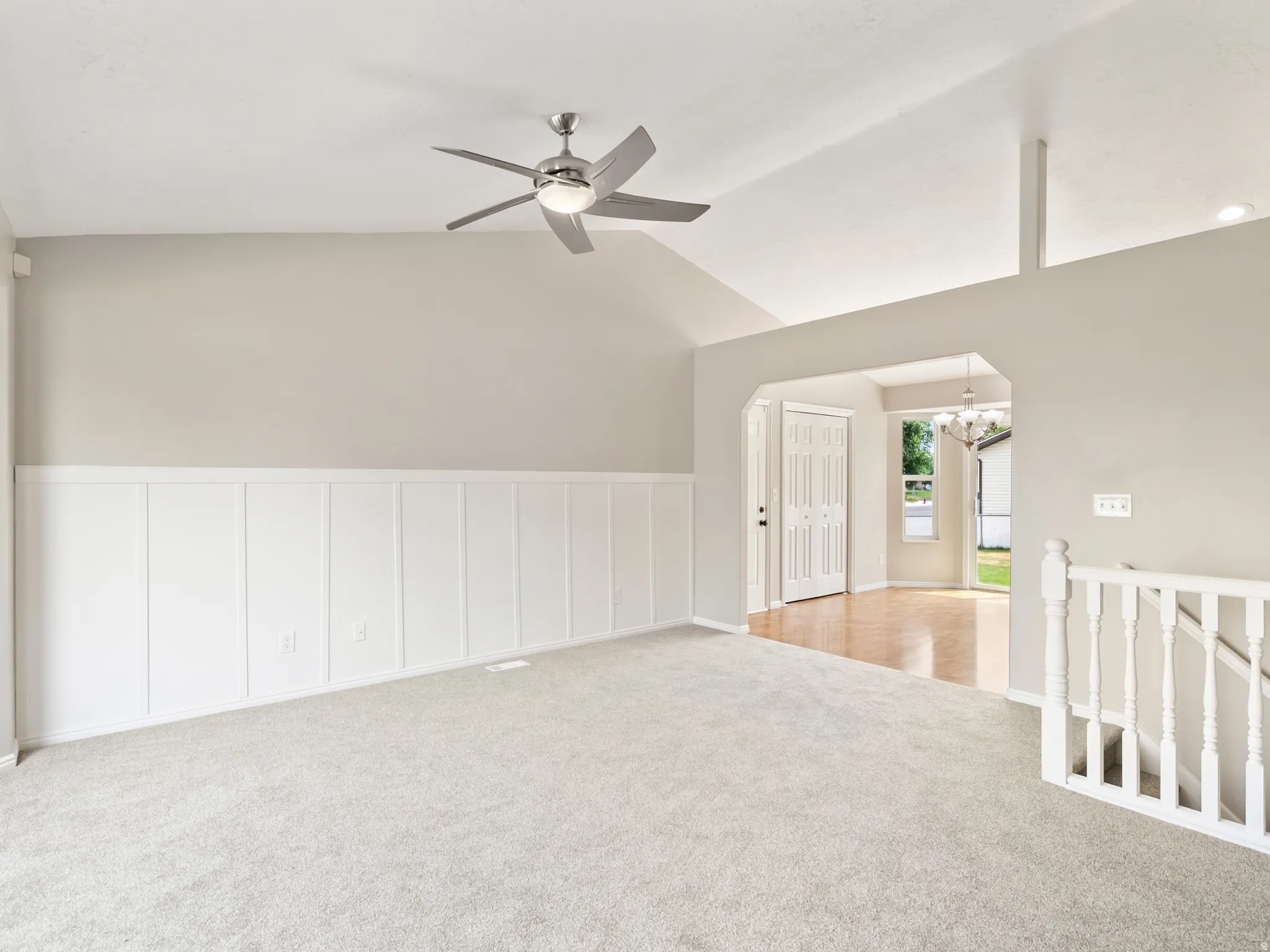 Living area featuring vaulted ceilings, board and batten wainscoting, and a ceiling fan with integrated lighting