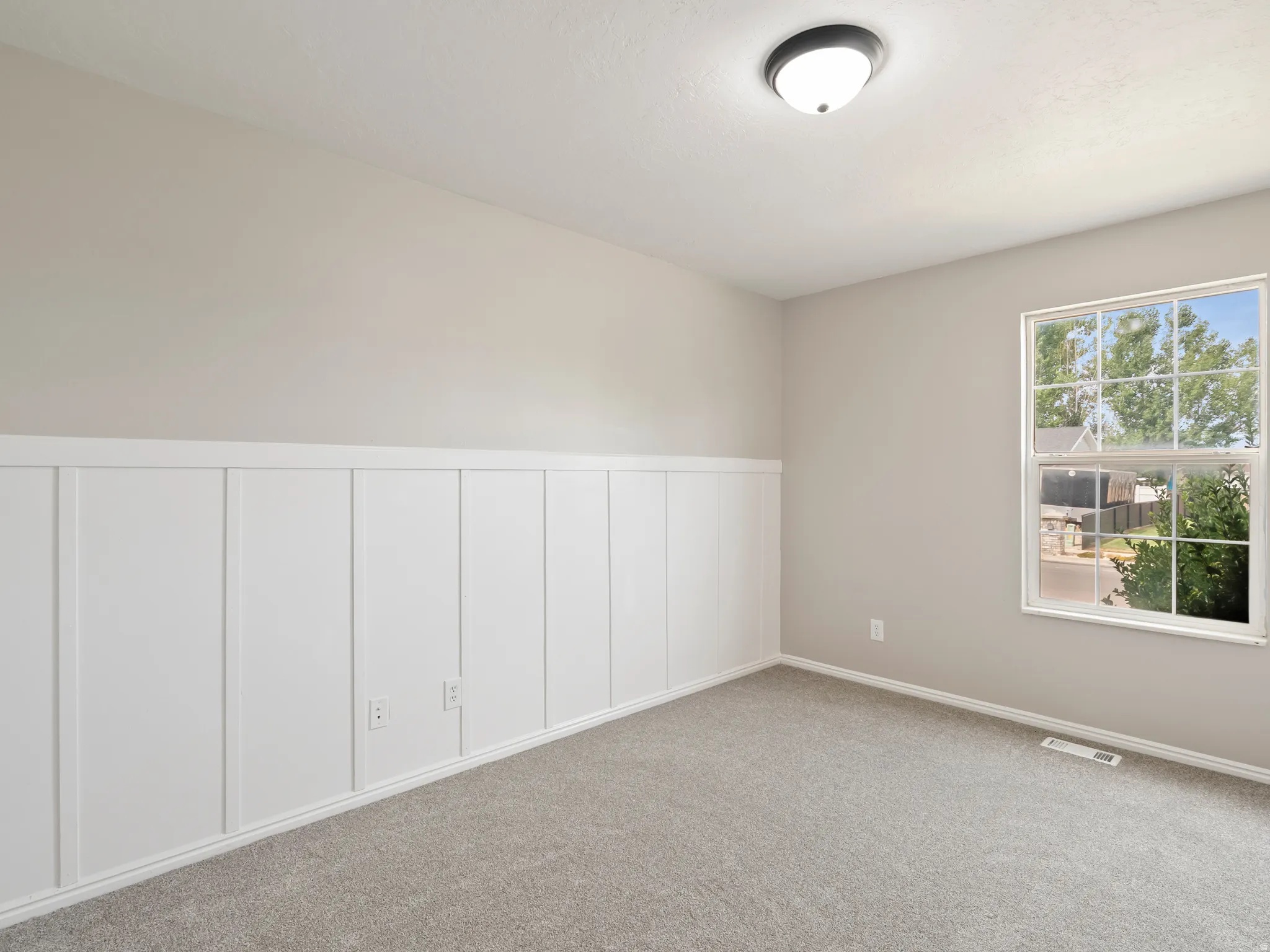 Interior room featuring wainscoting paneling, light gray carpeting, and a window with grid panes