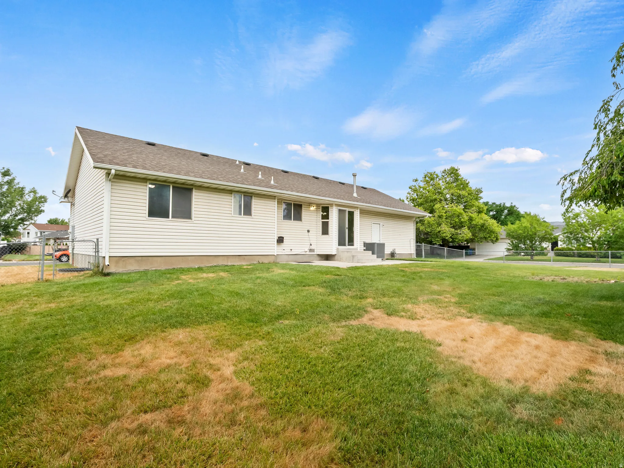Expansive backyard featuring a concrete patio, white vinyl siding, and a chain-link fence