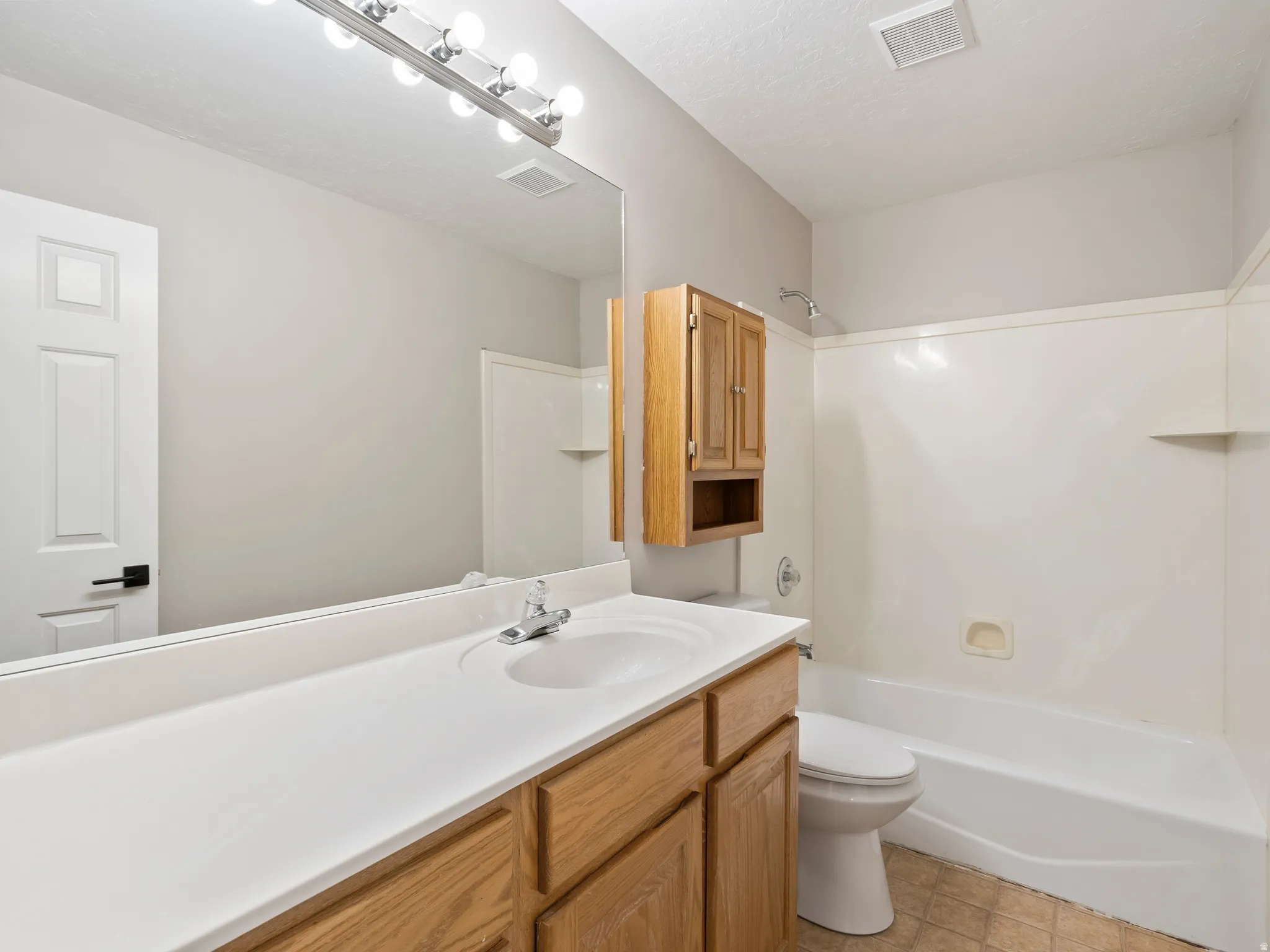 Bathroom featuring a single-sink vanity with white countertop and wood-finish cabinetry, a full-width mirror, and a bathtub with shower surround