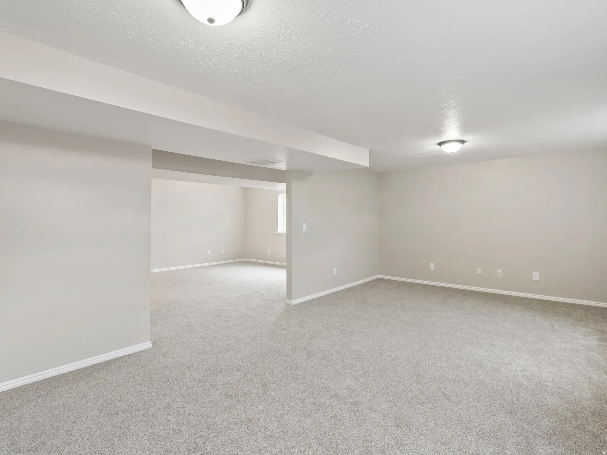 Spacious interior room featuring light gray carpeting, neutral-toned walls, and flush-mount ceiling lighting