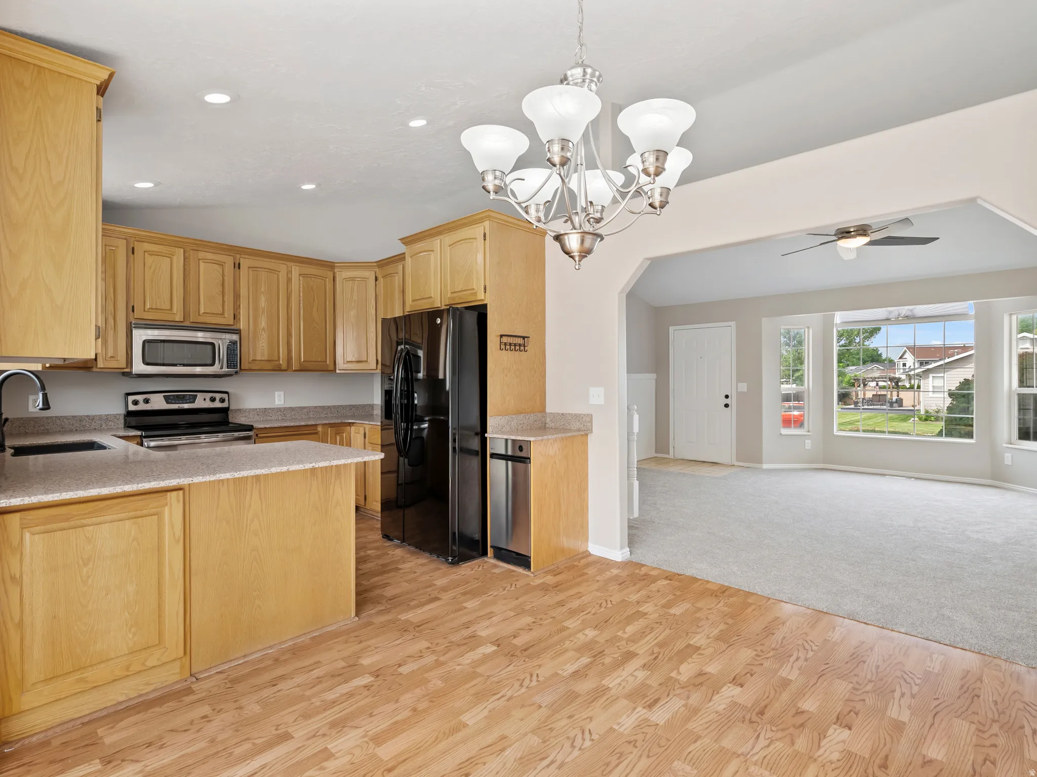 Open-concept kitchen featuring light wood cabinetry, stone-finish countertops, and stainless steel appliances